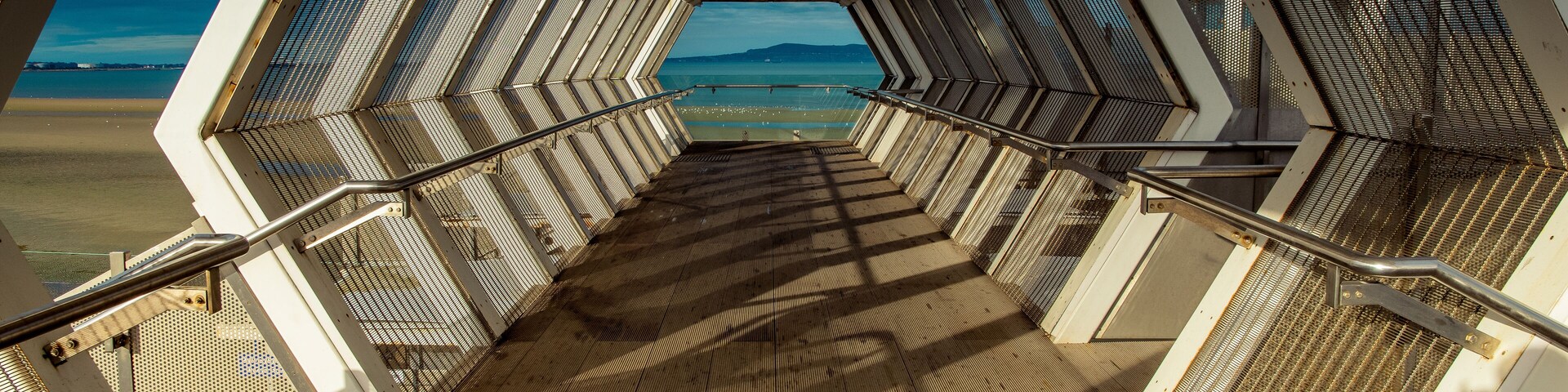 Modern polygon-shaped peatonal bridge in an Irish train station with a view at the beach.Booterstown dart station, Dublin, Ireland.