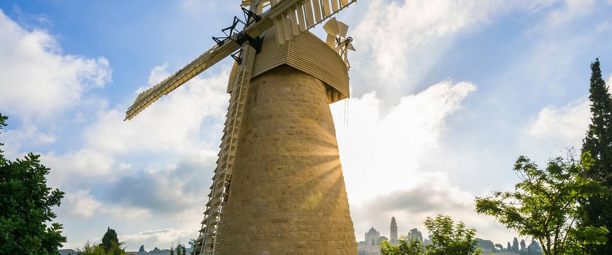 Un moulin à vent traditionnel, avec une base en pierre, se dressant sur fond de ciel dégagé et de bâtiments éloignés.