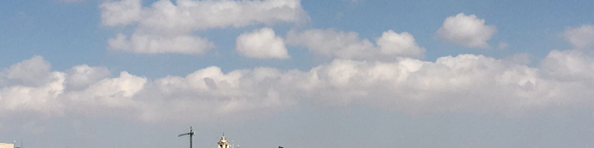 Un paisaje urbano denso con una imponente torre del reloj y un cielo azul despejado con algunas nubes.