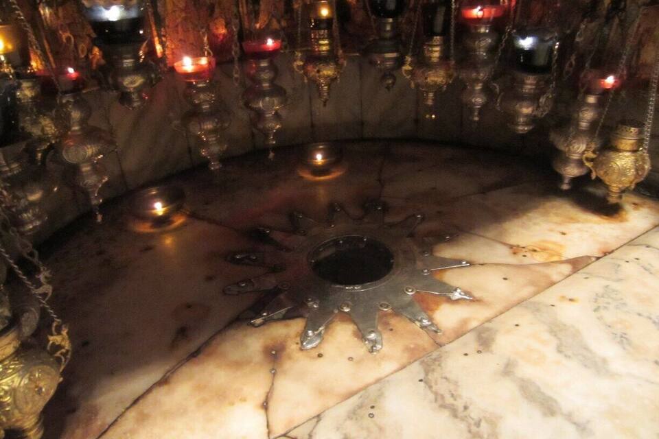 A sun-shaped metal object on a marble floor surrounded by ornate candle holders.