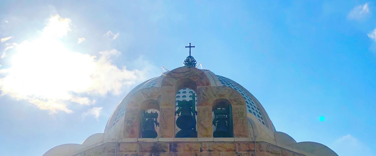 A large dome with a cross on top, a statue of an angel, and a clear blue sky with clouds.