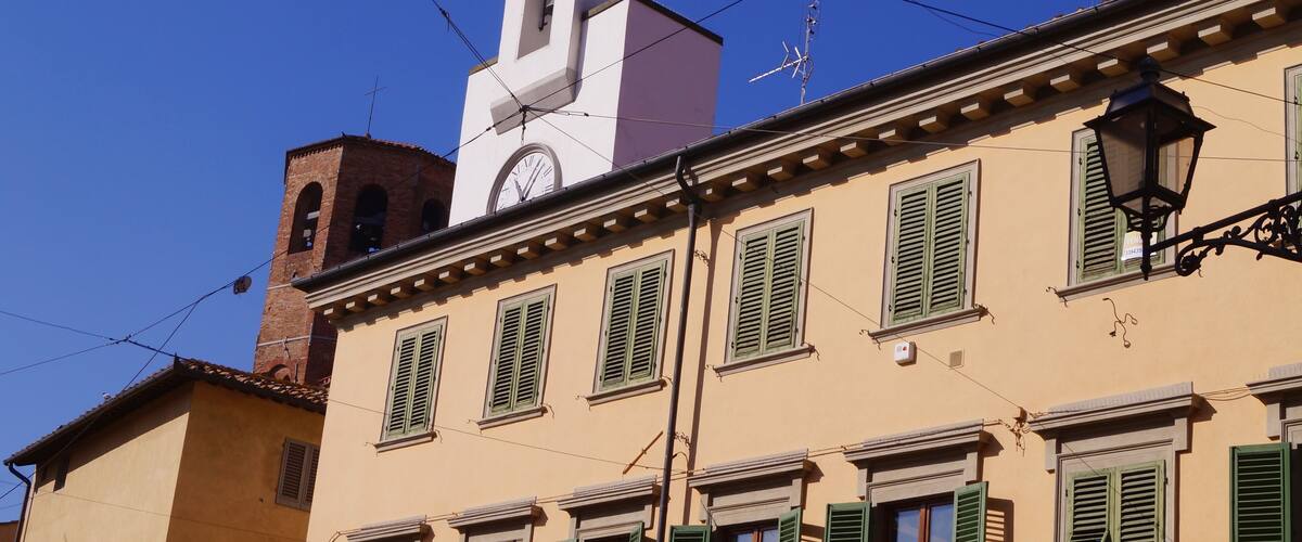 A building with a clock tower, green shutters, and a street lamp.
