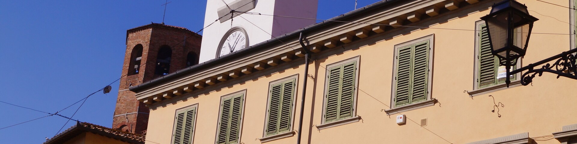 A building with a clock tower, green shutters, and a street lamp.