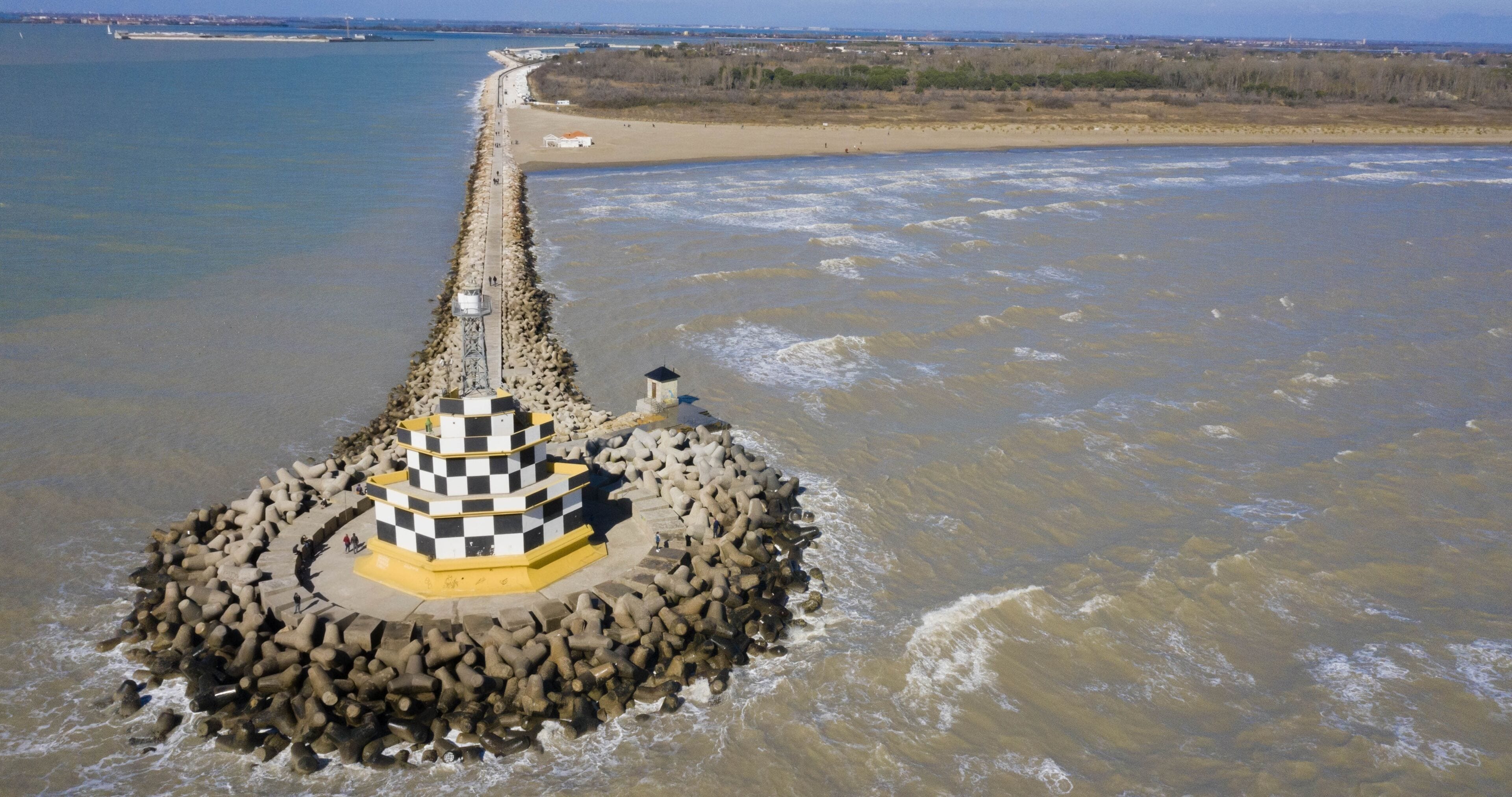 Un faro sobre un promontorio rocoso rodeado por una playa y un río.