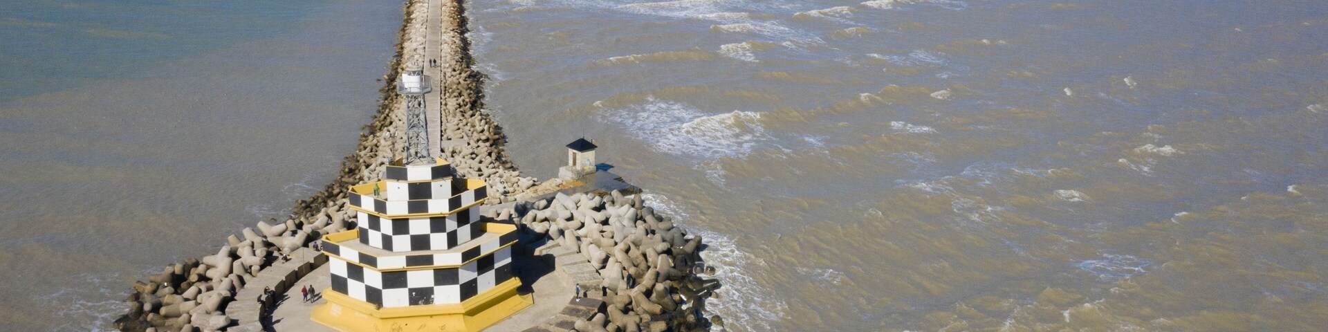 Un faro sobre un promontorio rocoso rodeado por una playa y un río.