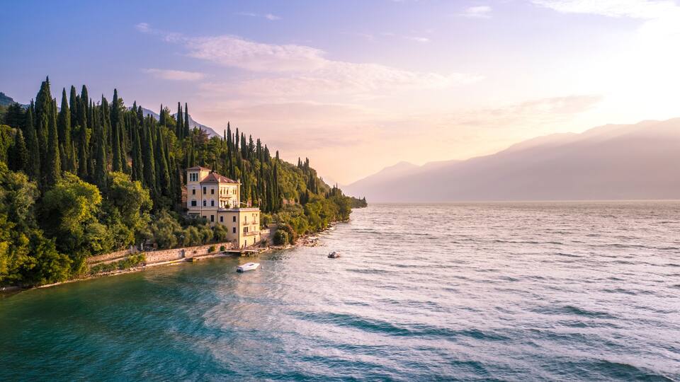 A coastal landscape with a building on a hillside, a body of water, and a distant mountain range.