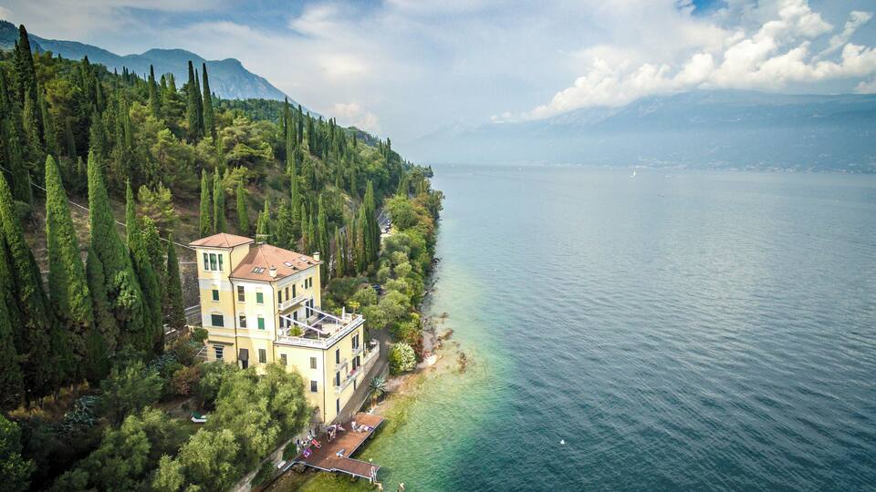 A lakeside villa surrounded by trees and mountains.