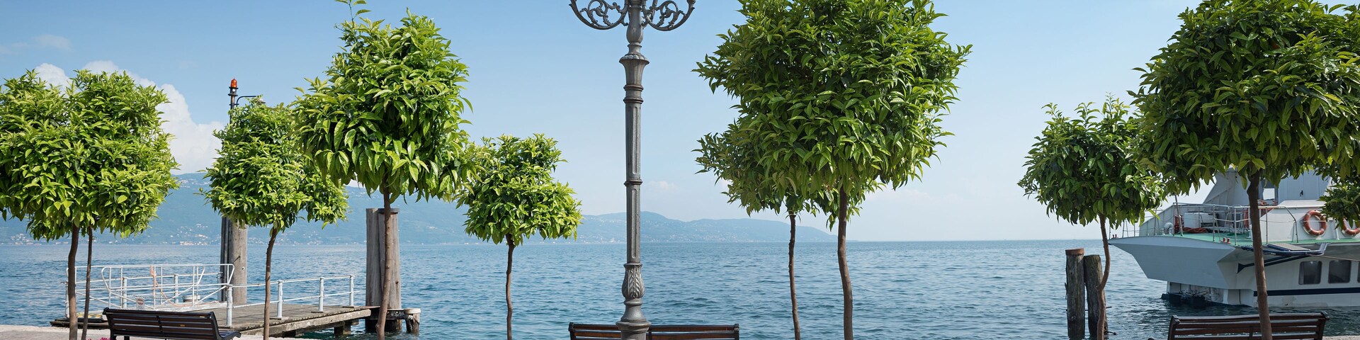 Um calçadão à beira-mar com bancos, um lampião e vegetação exuberante.