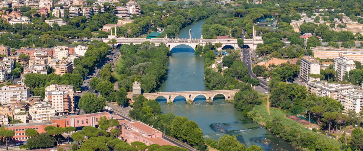Aerial view of the Tiber River featuring the historic Ponte Milvio and the modern Ponte Flaminio surrounded by lush green trees and urban architecture in Rome, Lazio, Italy.