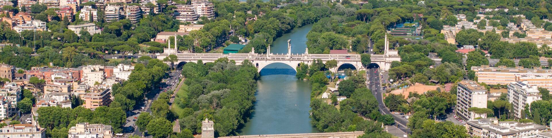 Aerial view of the Tiber River featuring the historic Ponte Milvio and the modern Ponte Flaminio surrounded by lush green trees and urban architecture in Rome, Lazio, Italy.