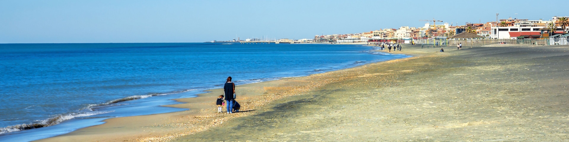 Uma praia com águas azul-claras, areal arenoso e edifícios ao fundo.