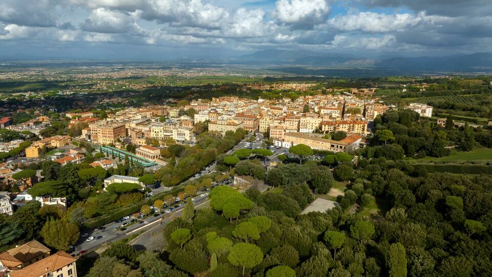 A panoramic view of a historic town with dense architecture, a prominent bridge, and rolling hills in the background.