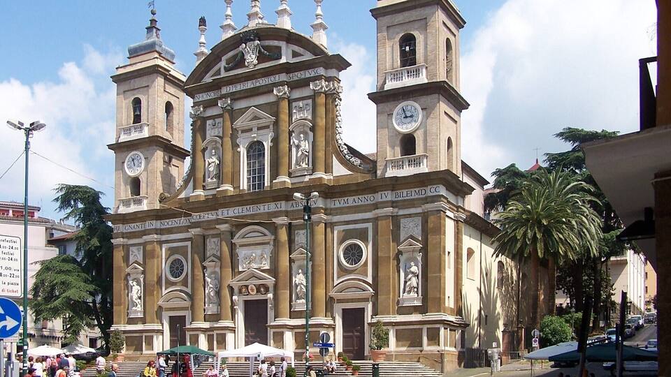 A historic church with two bell towers, a central dome, and statues.