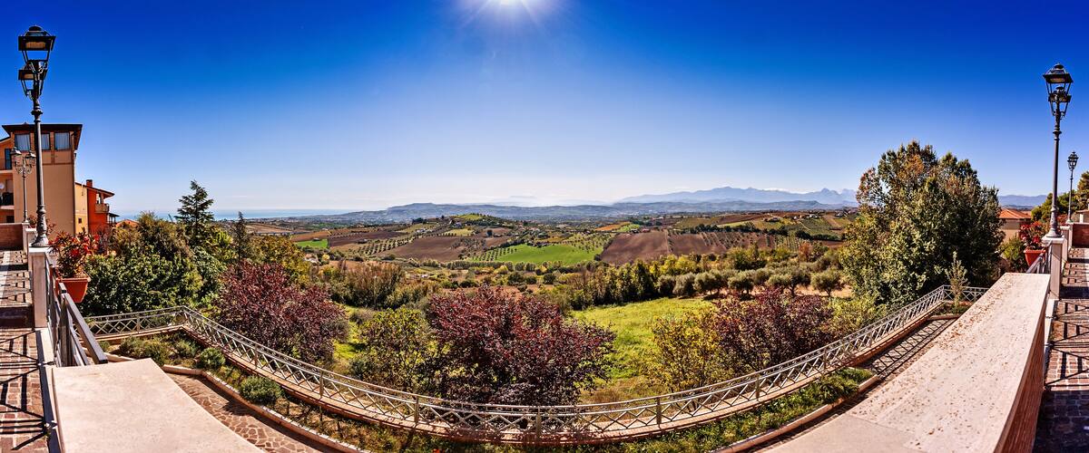A scenic view from a bridge overlooking a valley with mountains in the distance, under a clear blue sky.