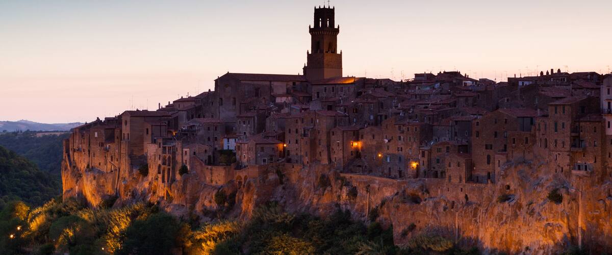 A historic fortified town with a prominent tower, surrounded by dense vegetation and illuminated buildings.