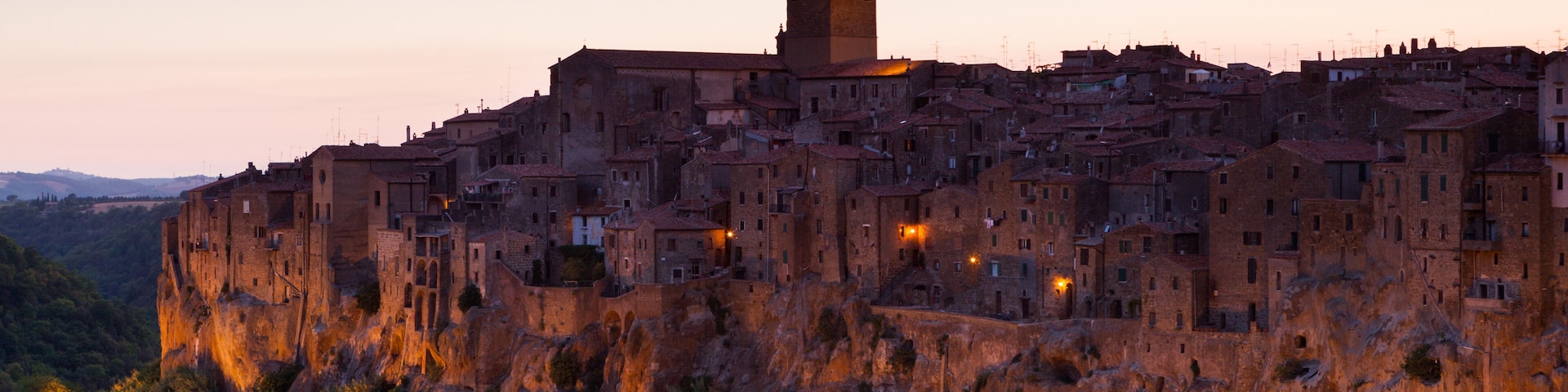A historic fortified town with a prominent tower, surrounded by dense vegetation and illuminated buildings.