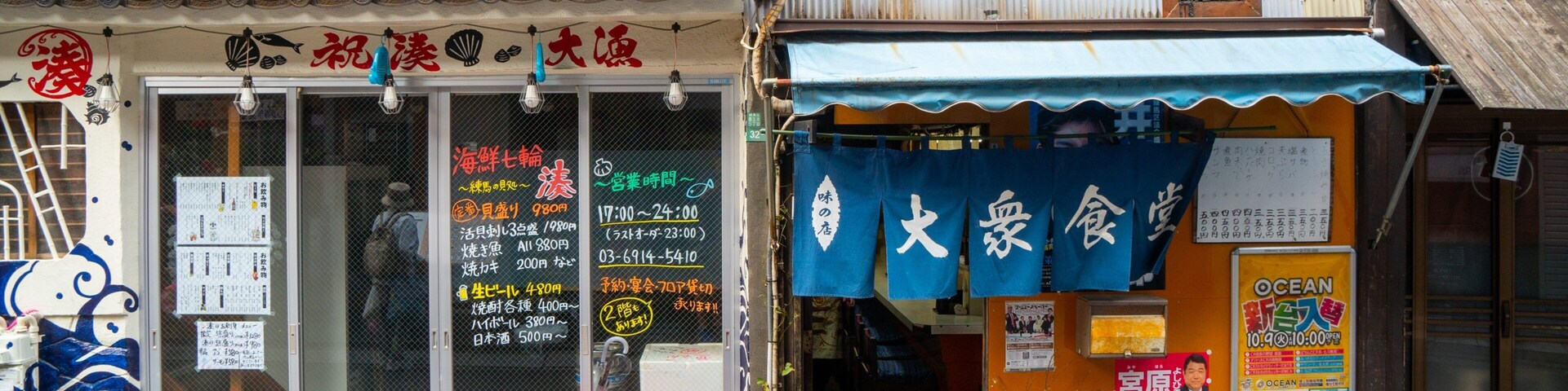 Un escaparate con un letrero en japonés, un toldo azul y una caja roja en el exterior.