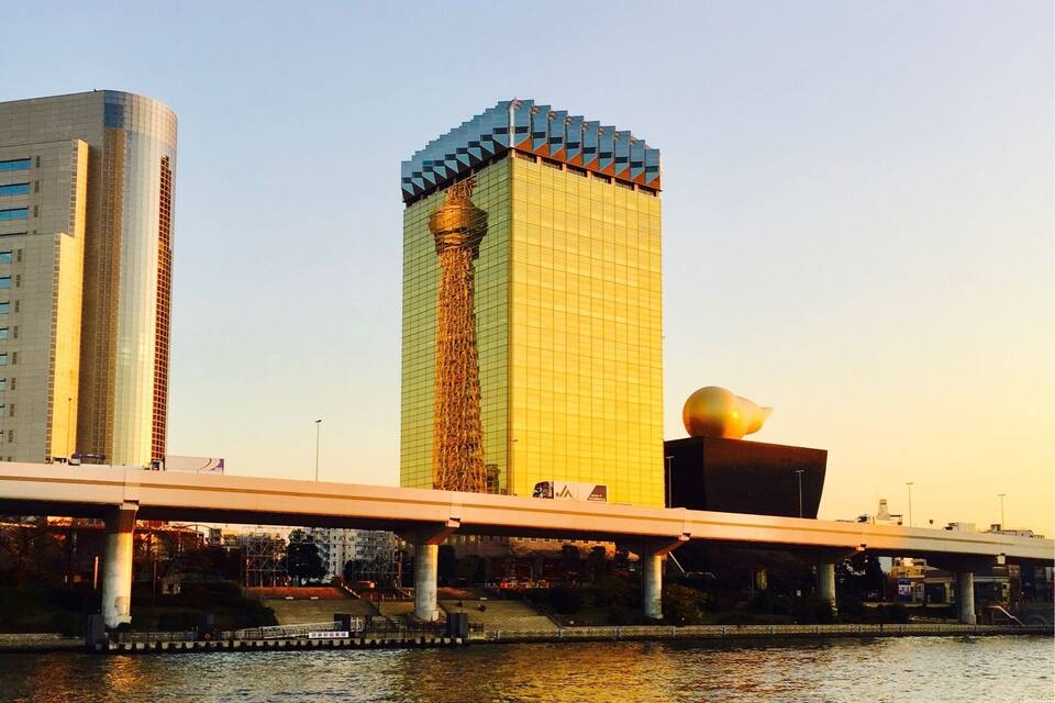 A modern cityscape with a prominent yellow building, a bridge over water, and a unique spherical sculpture.