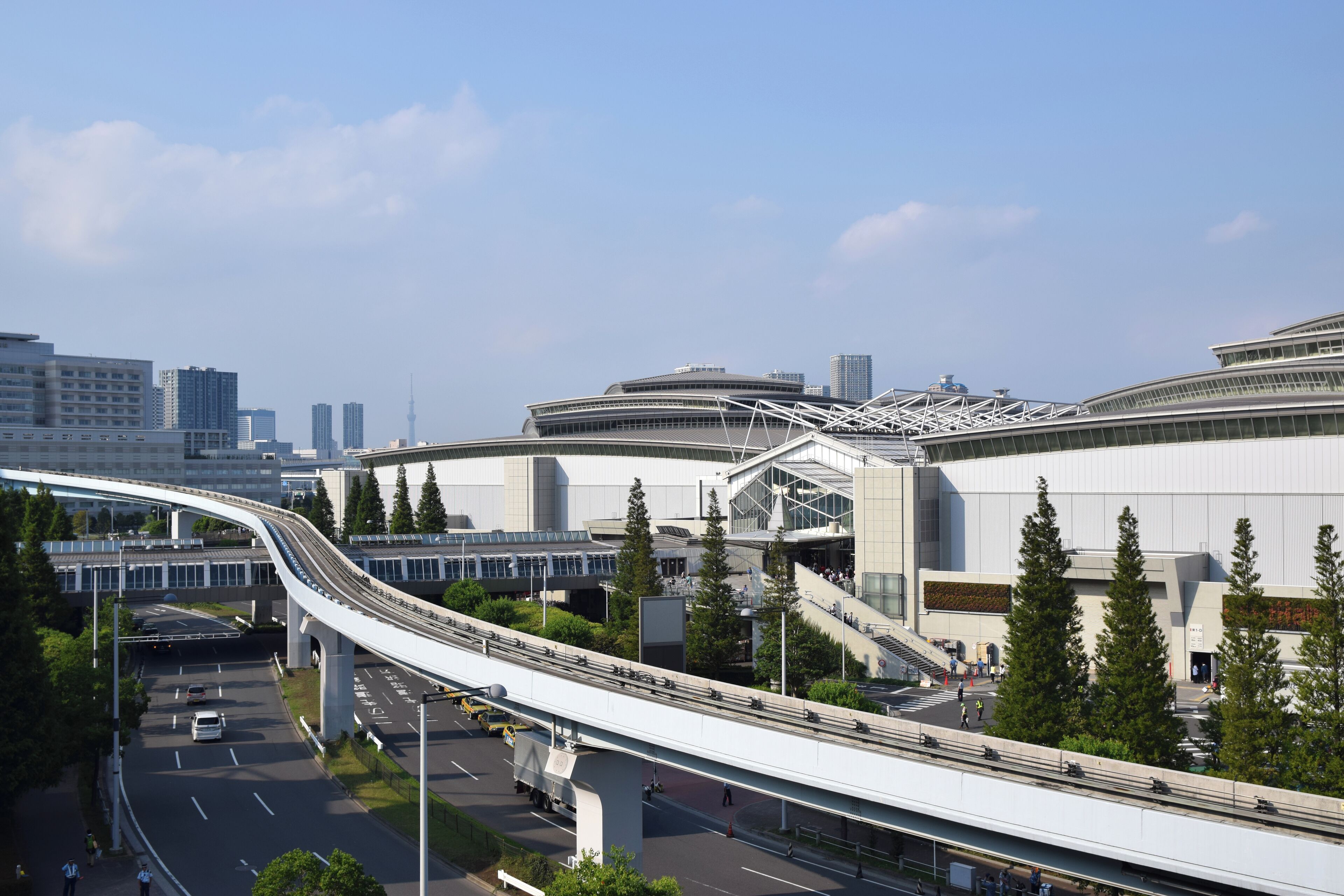 Paisagem urbana moderna com uma autoestrada elevada e curvilínea em destaque, um estádio grande e edifícios altos ao redor.