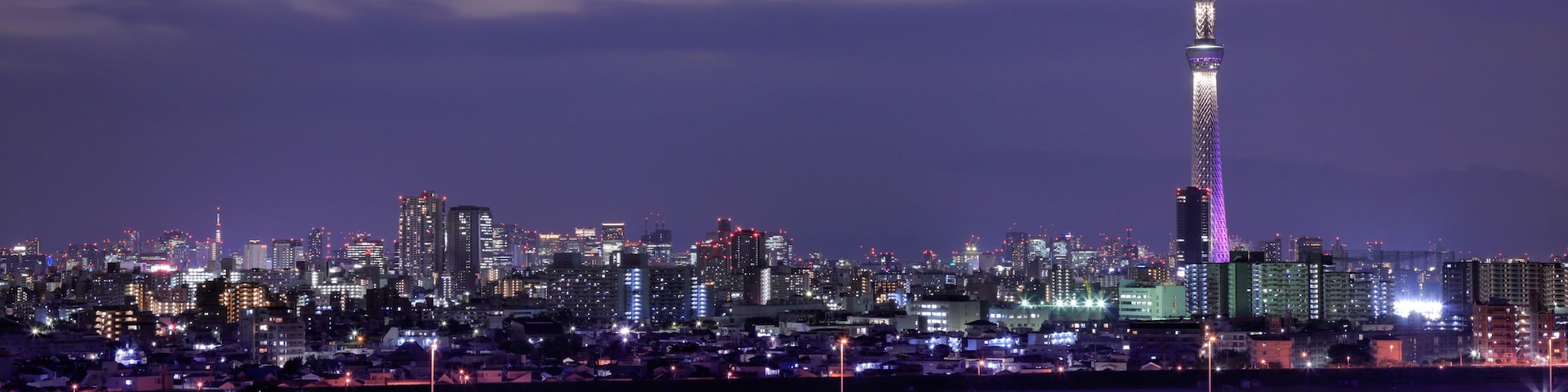 Silhueta urbana ao entardecer, com uma torre imponente iluminada no céu.