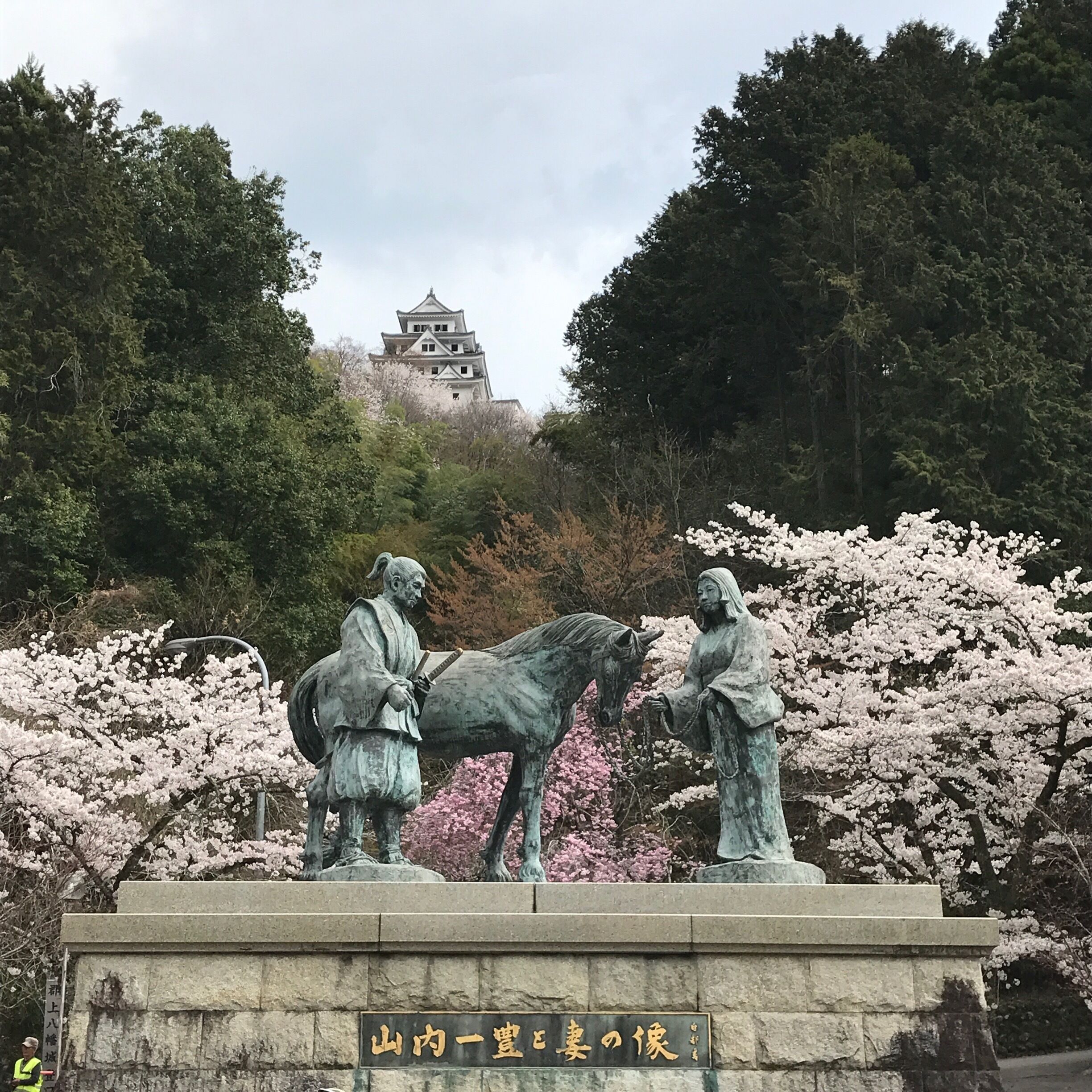 A statue of two figures with a horse, surrounded by cherry blossoms, with a castle in the background.