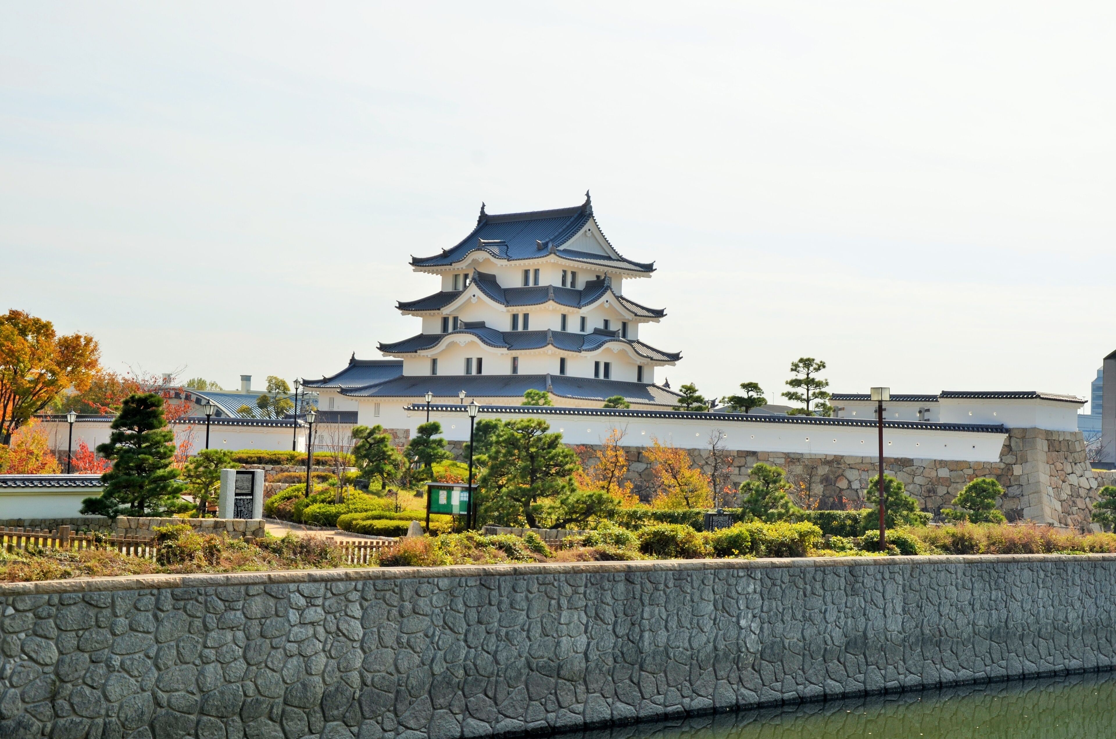 A traditional Japanese castle with multiple tiers, surrounded by a stone wall and lush greenery.