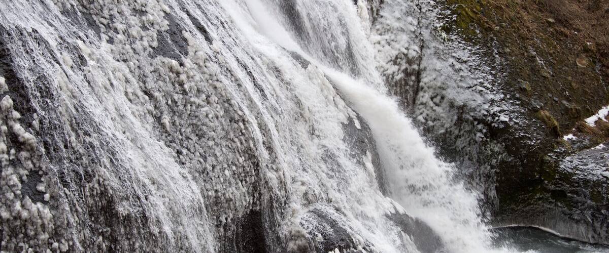 A waterfall cascading over rocks with snow patches.