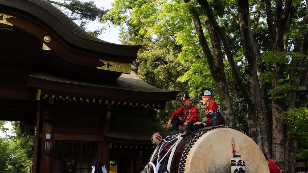 A traditional Japanese festival with participants in red attire, a large drum, and a shrine in the background.