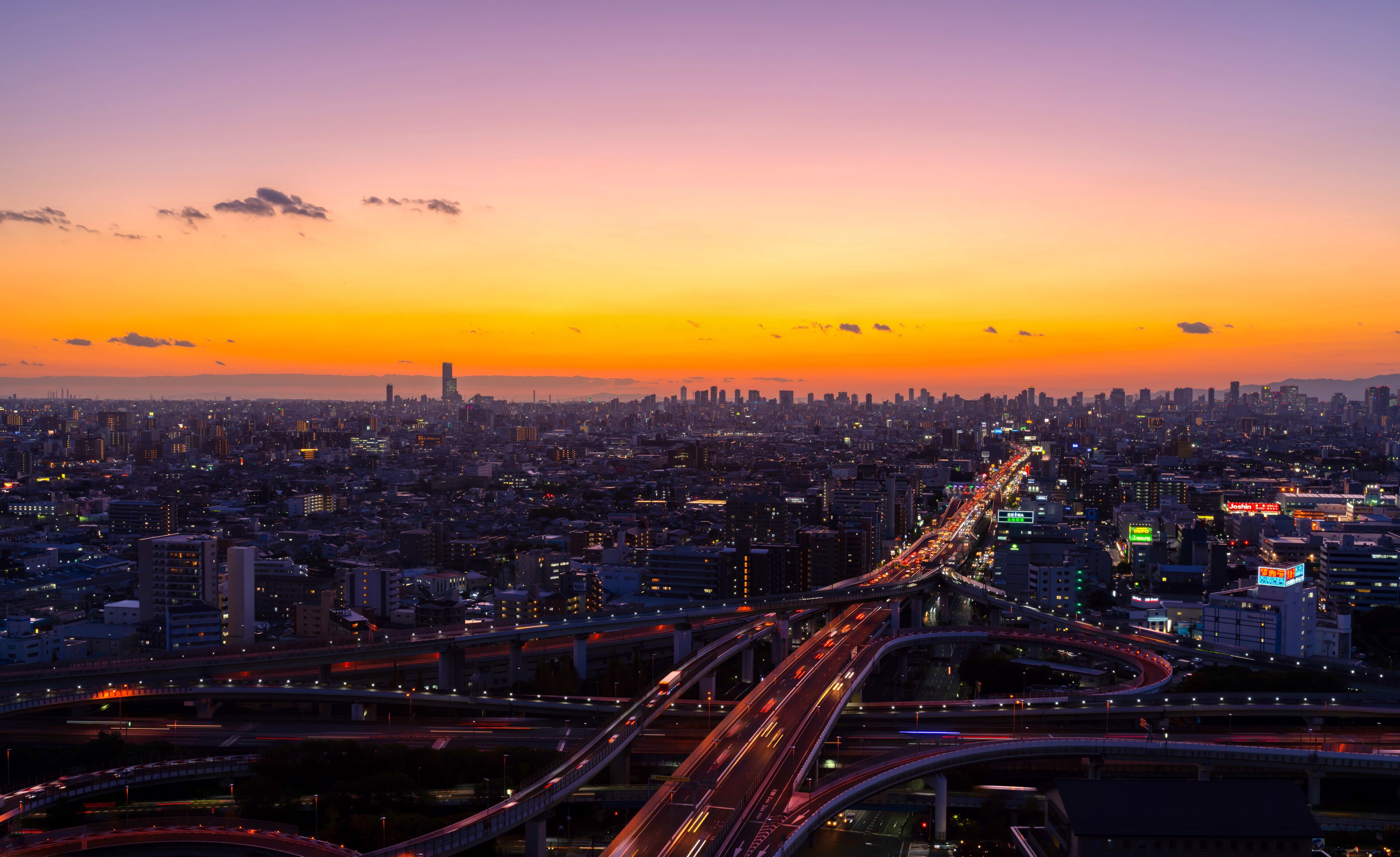 A cityscape at sunset with a prominent highway and dense urban buildings.