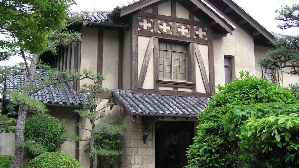 A traditional Japanese house with a tiled roof, wooden beams, and a window with a lattice design.
