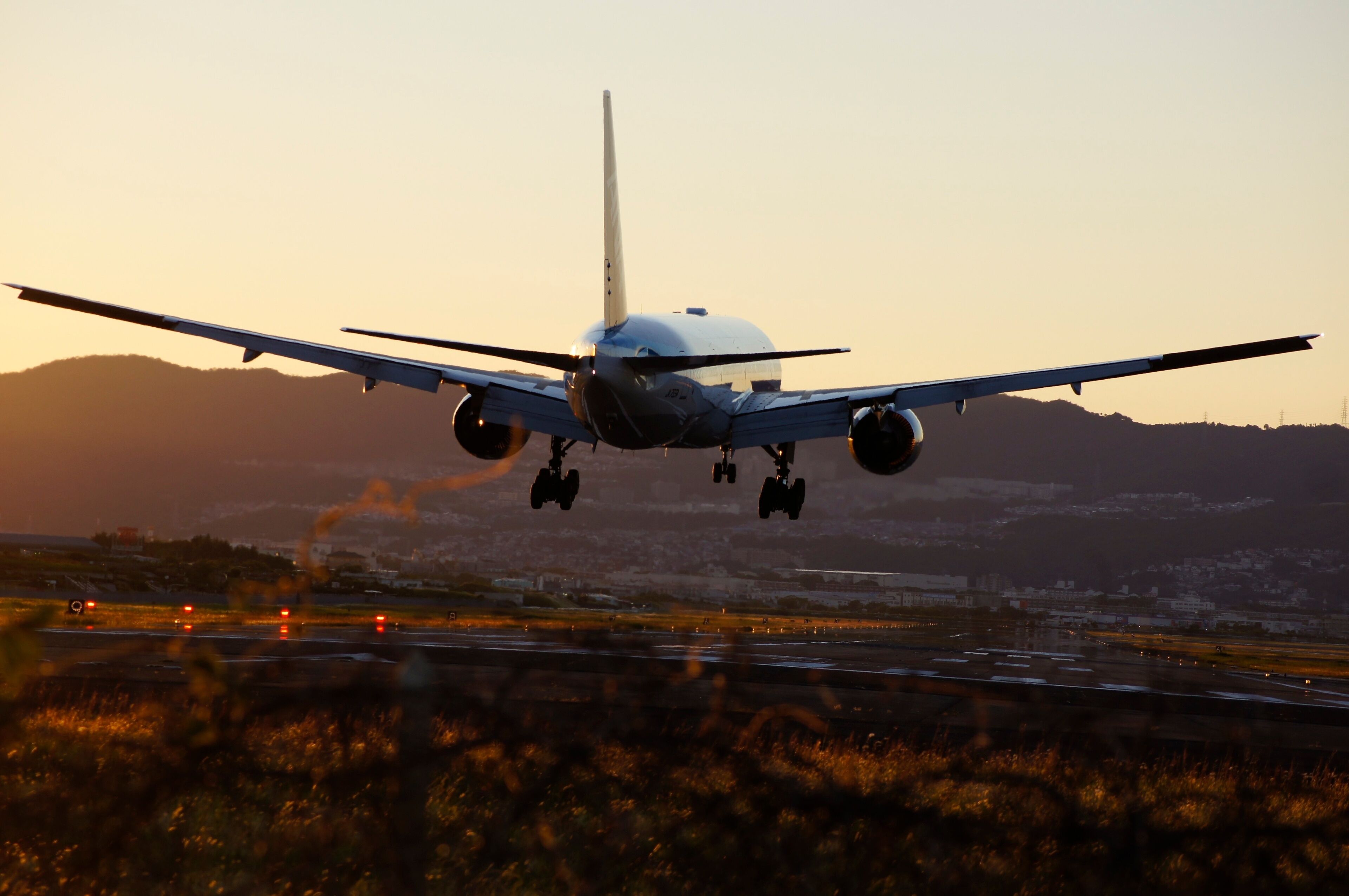 An airplane landing with its landing gear extended, approaching a runway with a mountainous backdrop.