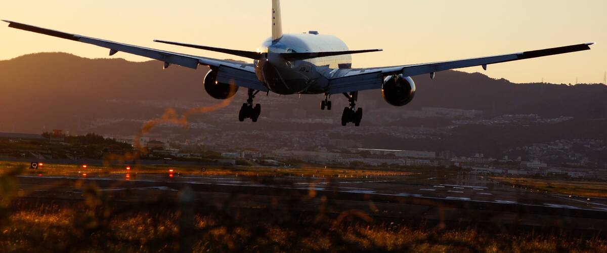 An airplane landing with its landing gear extended, approaching a runway with a mountainous backdrop.