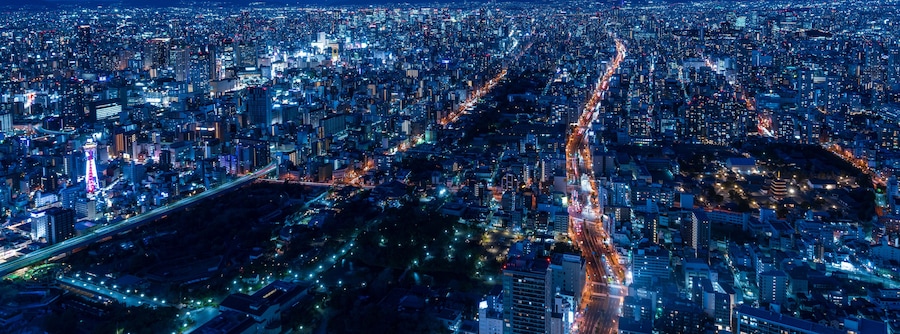 Un paisaje urbano nocturno y concurrido, con numerosos edificios iluminados y calles llenas de movimiento.