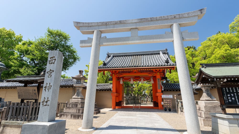 A traditional Japanese torii gate with a stone pillar inscription, a tiled roof, and a stone pathway leading to a shrine.