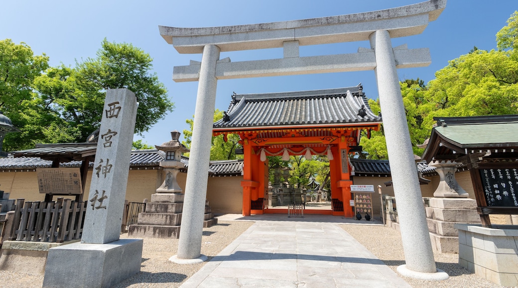 A traditional Japanese torii gate with a stone pillar inscription, a tiled roof, and a stone pathway leading to a shrine.