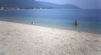 A beach with clear water, a person in the water, and mountains in the background.