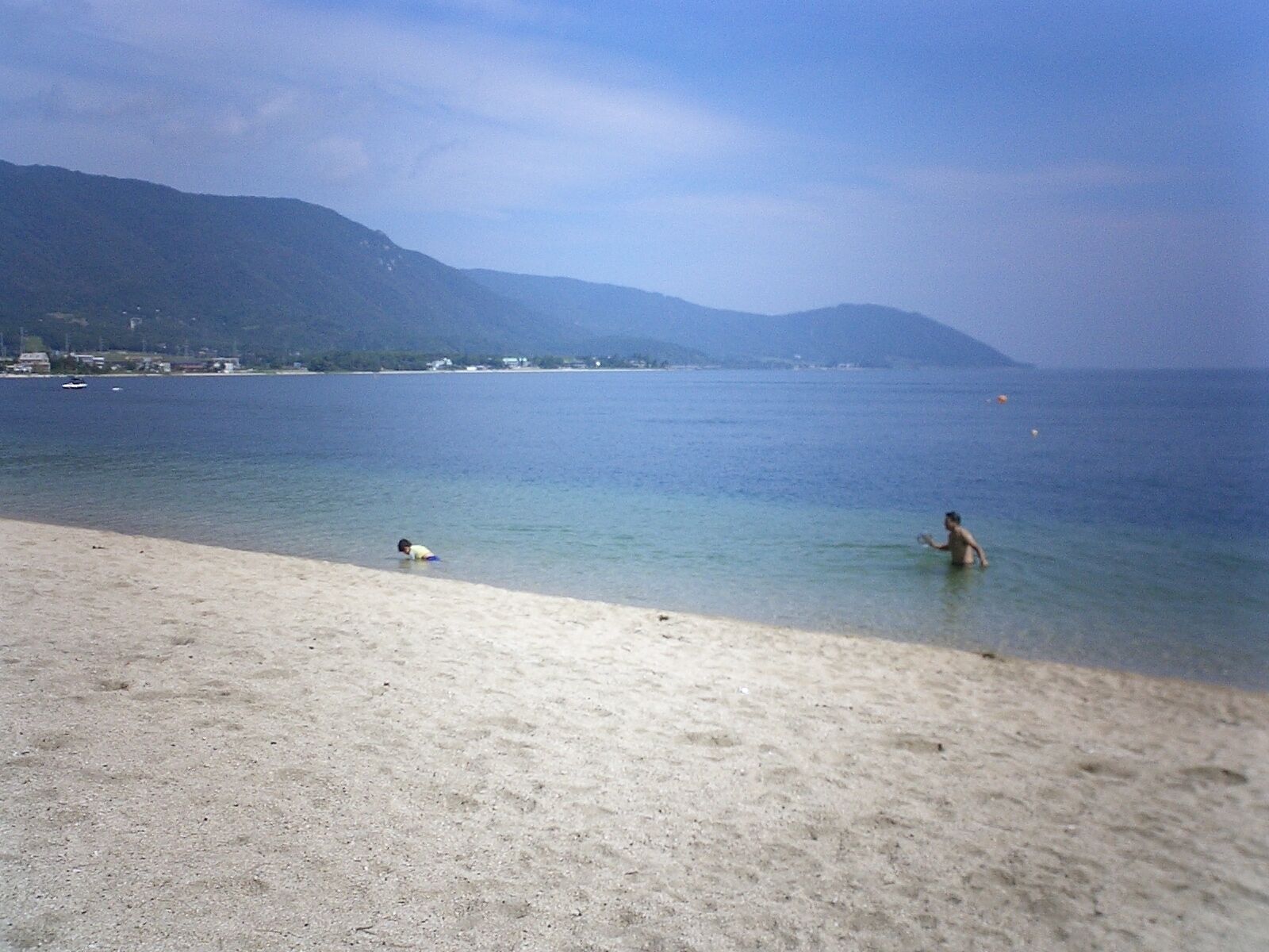 A beach with clear water, a person in the water, and mountains in the background.