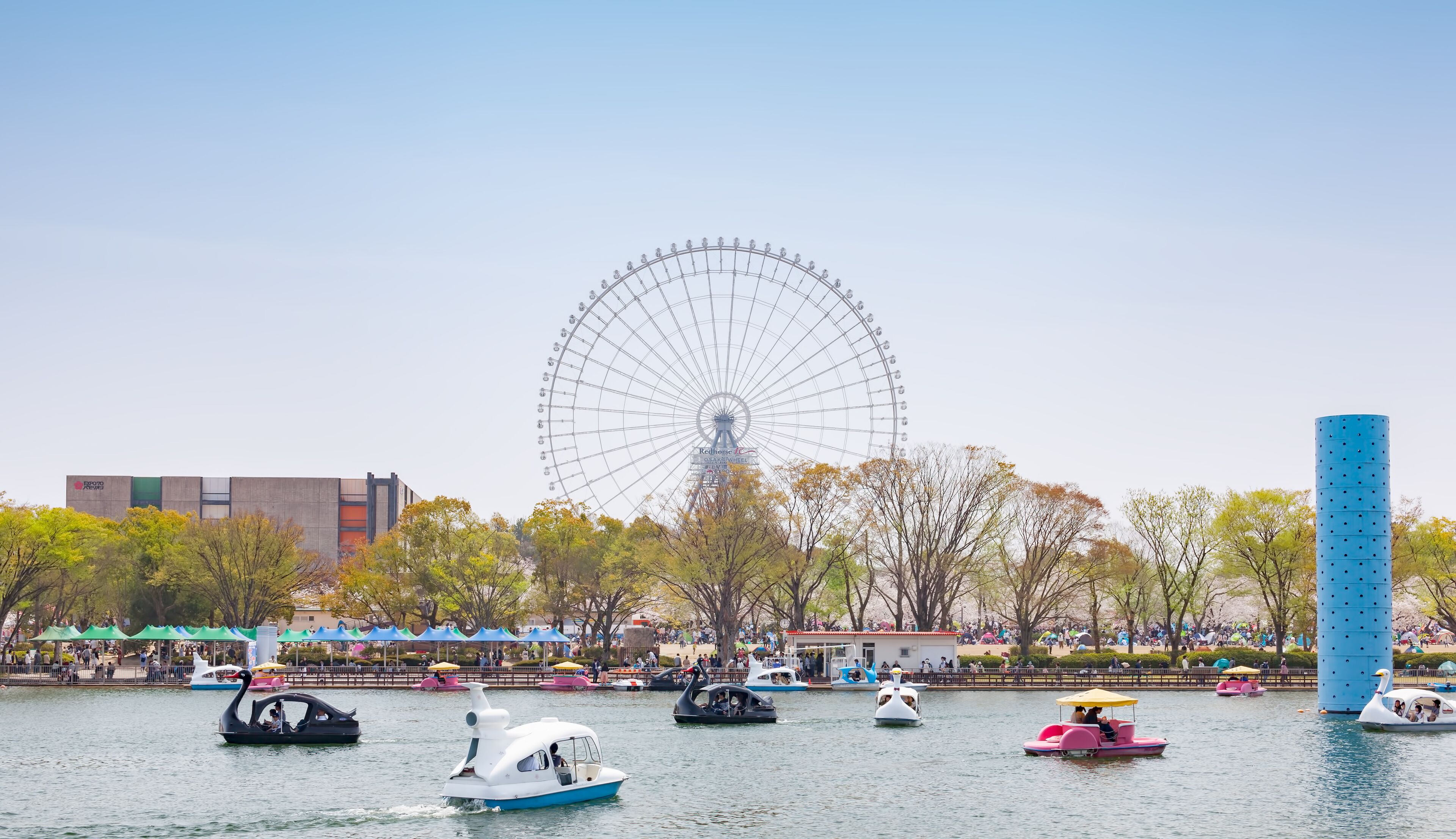 A Ferris wheel, a body of water with boats, and a blue tower.