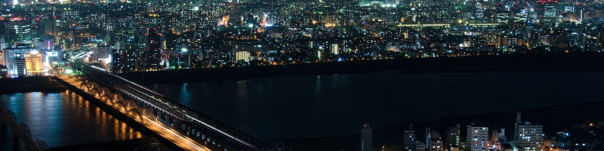 Paisagem urbana noturna com rio, edifícios iluminados e uma ponte.
