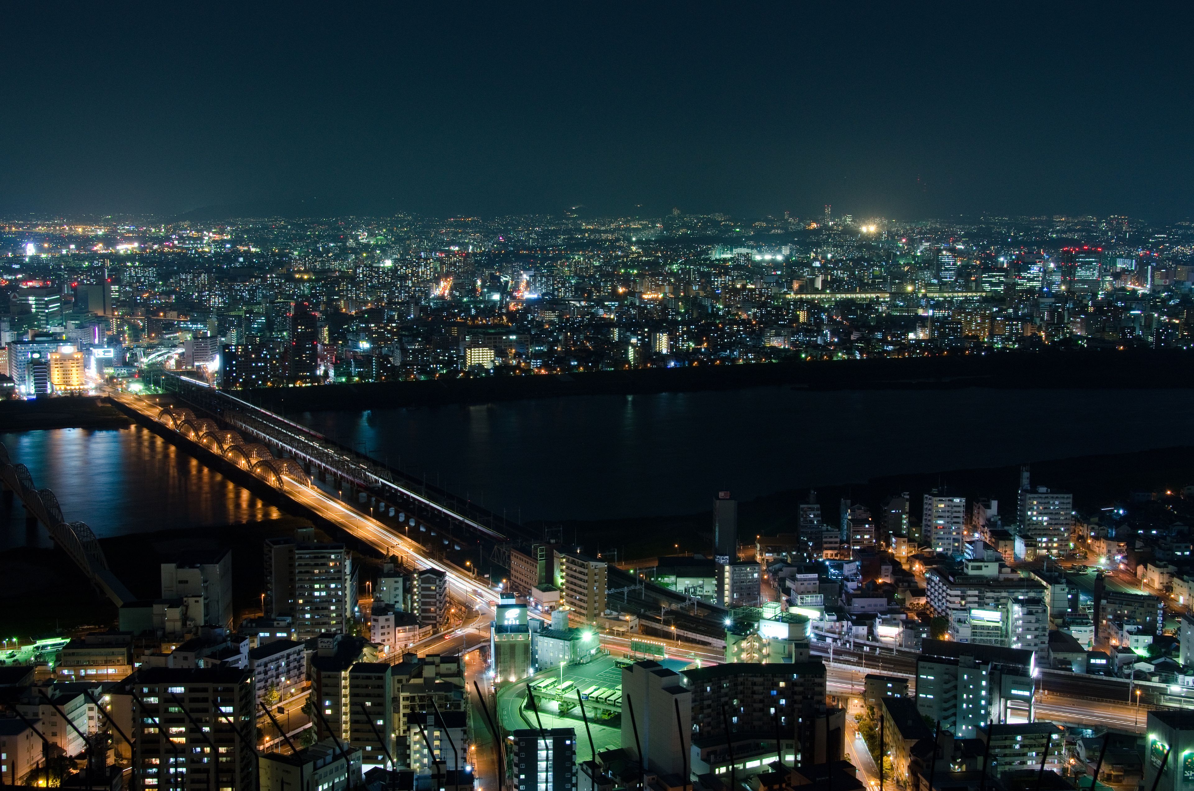 A nighttime cityscape with a river, illuminated buildings, and a bridge.