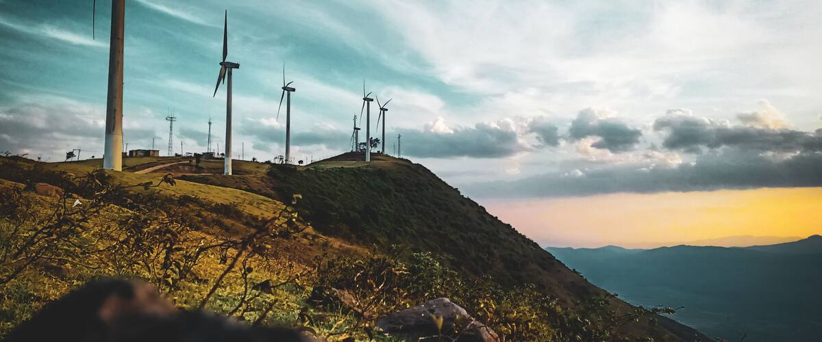Wind turbines on a hill with a cloudy sky.