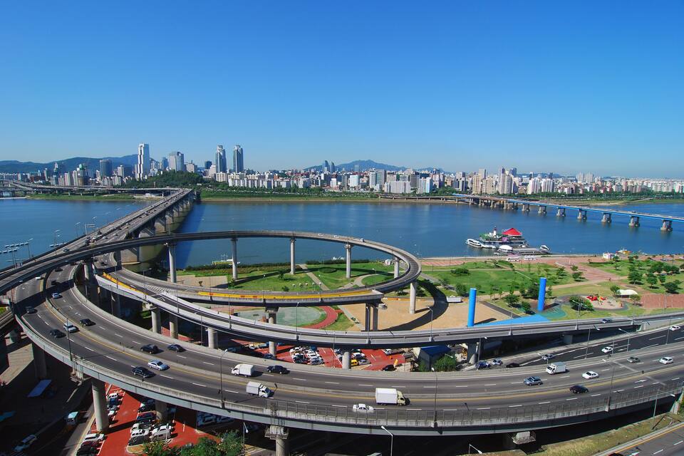 A multi-level highway interchange with a river and city skyline in the background.