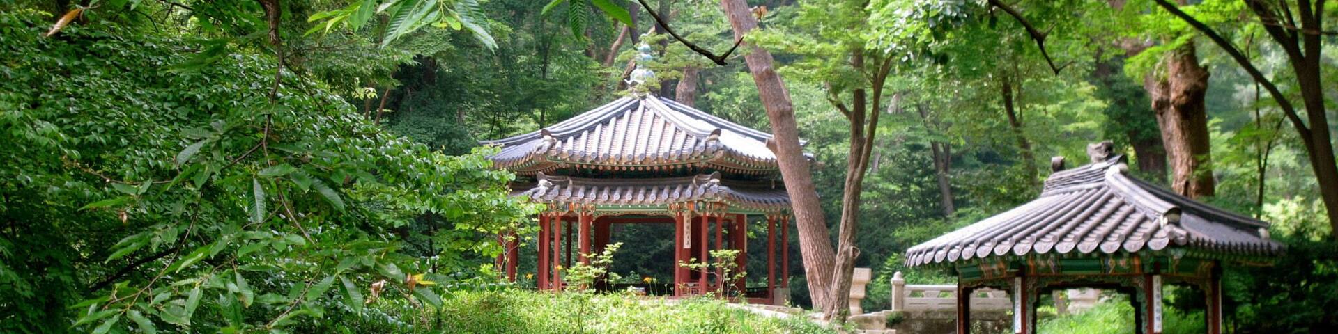 A traditional pavilion by a calm pond surrounded by lush greenery.