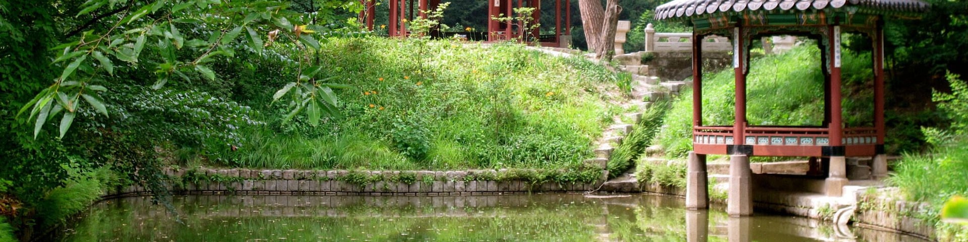 A traditional pavilion by a calm pond surrounded by lush greenery.