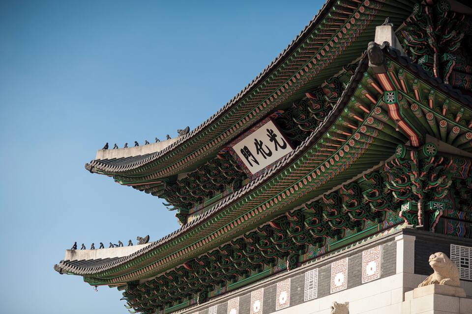 A traditional Chinese building with ornate green and red roof tiles and a large white sign with black Chinese characters.