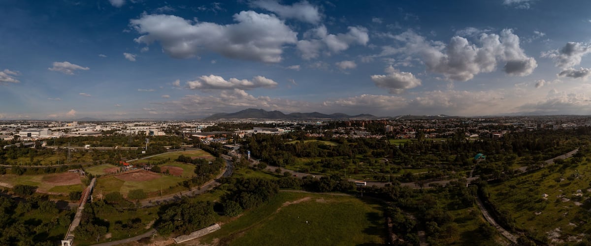 A panoramic view of a city with a park, mountains, and a clear sky.