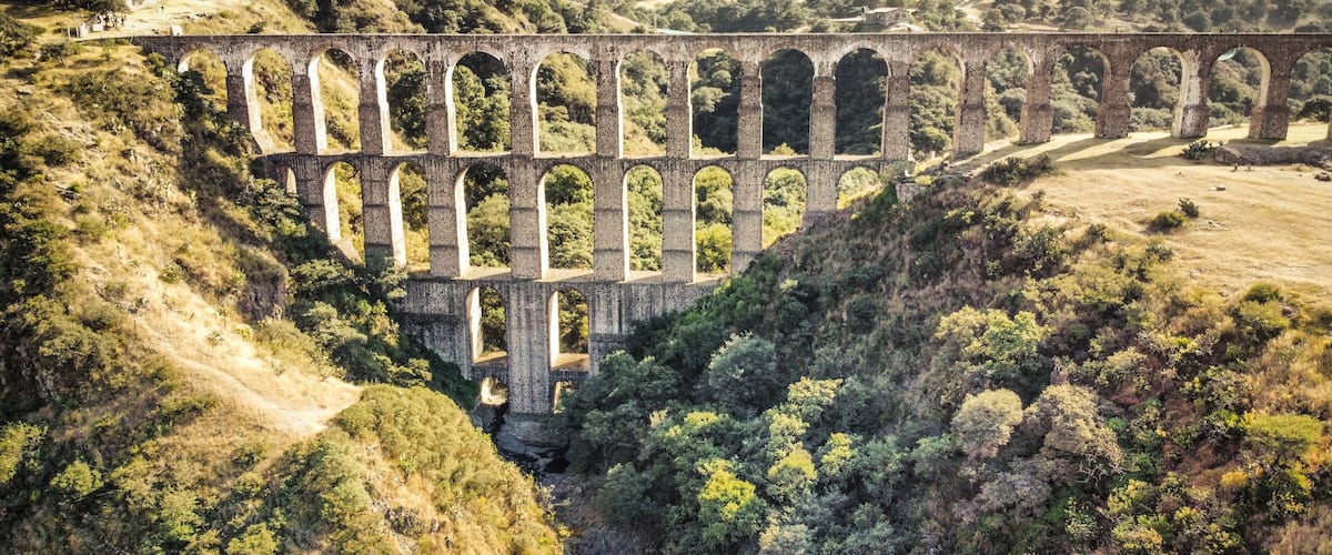 A large stone viaduct spanning a valley with lush greenery and hills in the background.