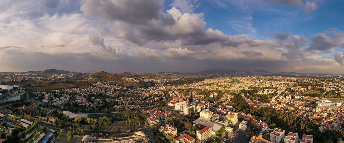 A panoramic view of a city with a large stadium, residential areas, and mountains in the background.