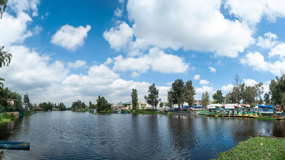 A calm river with boats, trees, and buildings along the banks.