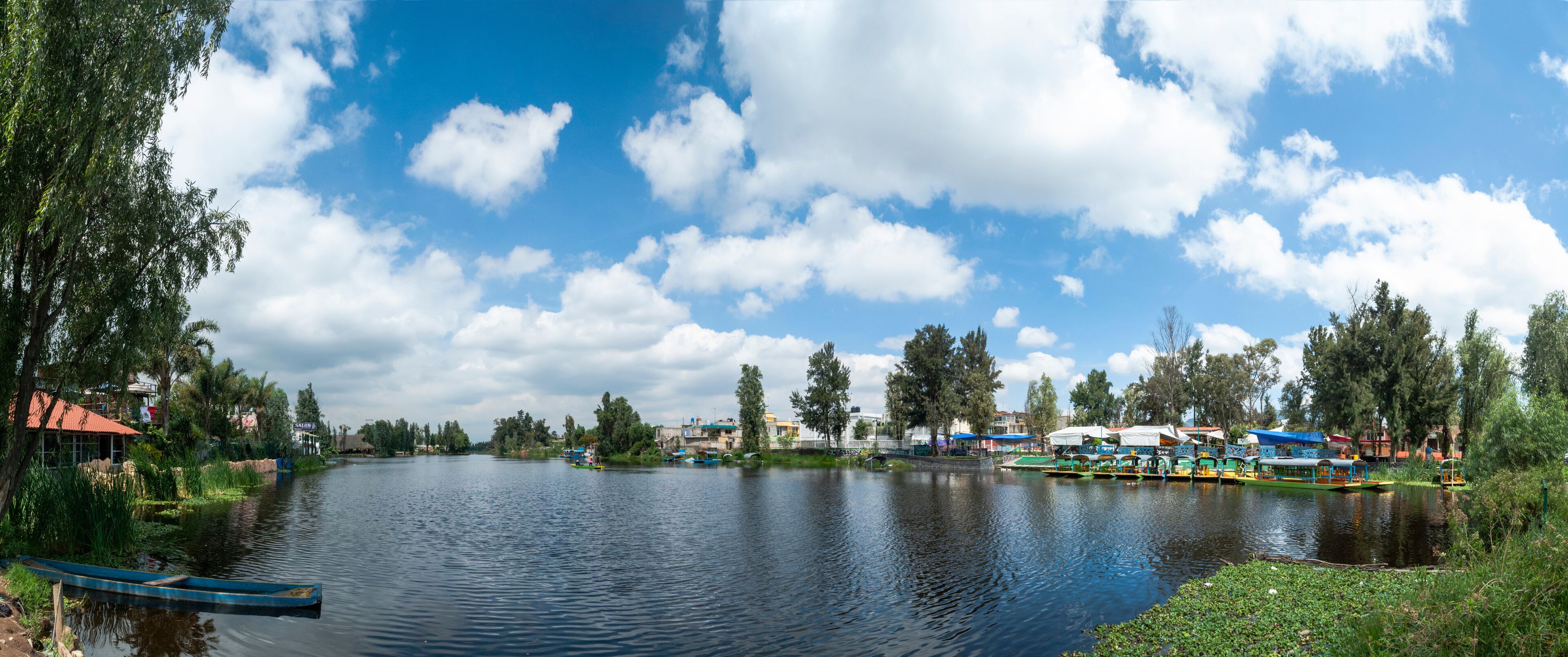 A calm river with boats, trees, and buildings along the banks.